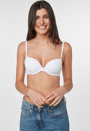 Sutien alb căptușit cu bretele ajustabile, material neted și design cu închidere frontală, asortat cu blugi din denim albastru cu talie înaltă.