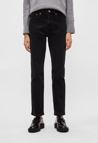 Melns džinsa auduma džinsi ar taisnu griezumu, aprīkoti ar vara krāsas detaļām, piecām kabatām un vieglu faktūru. Kombinēti ar spīdīgi melniem apaviem.