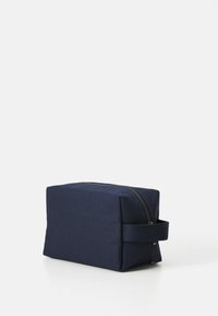 Trousse de toilette rectangulaire en tissu bleu marine avec une fermeture éclair sur le dessus et une poignée latérale, sur fond blanc.