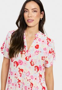 Vestido floral con un fondo claro decorado con flores rojas y rosas, mangas cortas, escote en V y un fondo fluido.