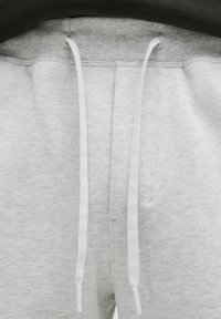 Pantalons de survêtement gris avec une texture douce, dotés d'une fermeture à cordon de serrage avec des embouts blancs, et d'une taille côtelée.
