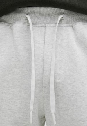 Pantalons de survêtement gris avec une texture douce, dotés d'une fermeture à cordon de serrage avec des embouts blancs, et d'une taille côtelée.