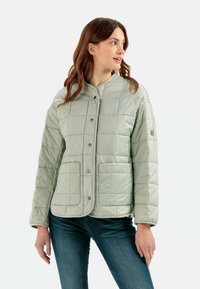 Hellgrüne gesteppte Jacke mit rundem Halsausschnitt, Druckknöpfen und zwei vorderen Taschen. Glatte Textur mit einem leicht glänzenden Finish.