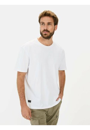 Weißes T-Shirt mit kurzen Ärmeln aus Baumwolle, mit rundem Ausschnitt und einem kleinen schwarzen Etikett in der unteren linken Ecke.