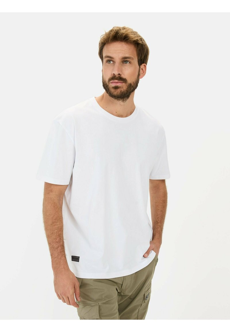 Hvid kortærmet T-shirt lavet af bomuld, med rund hals og et lille sort mærke i nederste venstre hjørne.