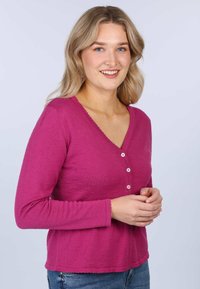 Fuchsia long-sleeve V-neck t-shirt with four white buttons at the front, textured fabric, and scalloped hemline.