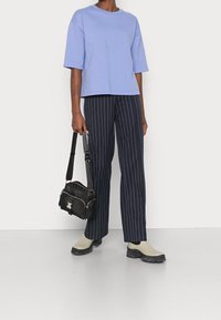 T-shirt oversized viola chiaro, pantaloni a gamba larga a righe blu navy, borsa a tracolla nera con hardware in argento e scarpe slip-on beige con suole spesse.