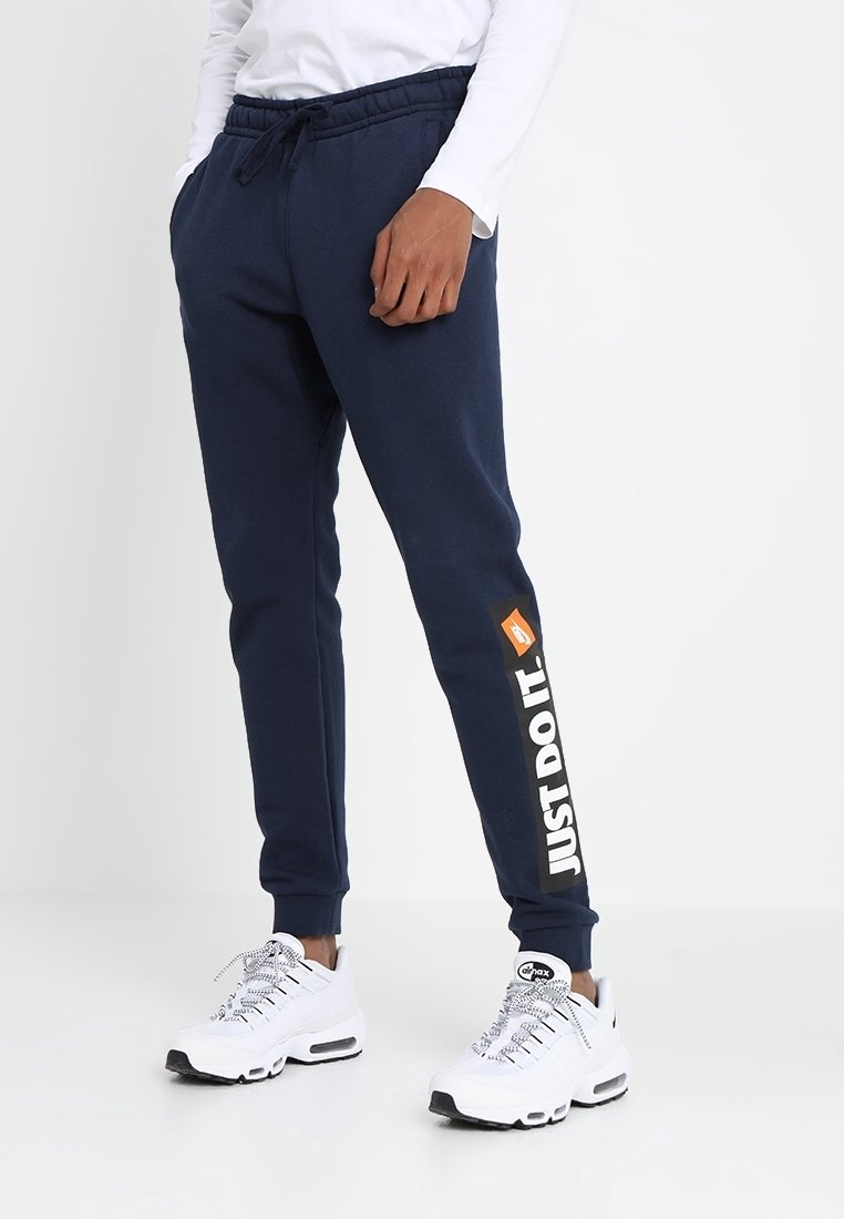 Mörkblå joggarbyxor med resårmidja, sidofickor och texten "JUST DO IT." på vänster ben. Matchat med vita sneakers.