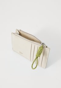 Portofel din piele bej, cu închidere cu fermoar, cu multiple sloturi pentru carduri și o bandă de tragere cu un model verde. Textură netedă și formă rectangulară.