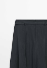 Sort nederdel med høj talje, syede bæltestropper og synlig lynlåslukning bagpå, lavet af let vævet stof.