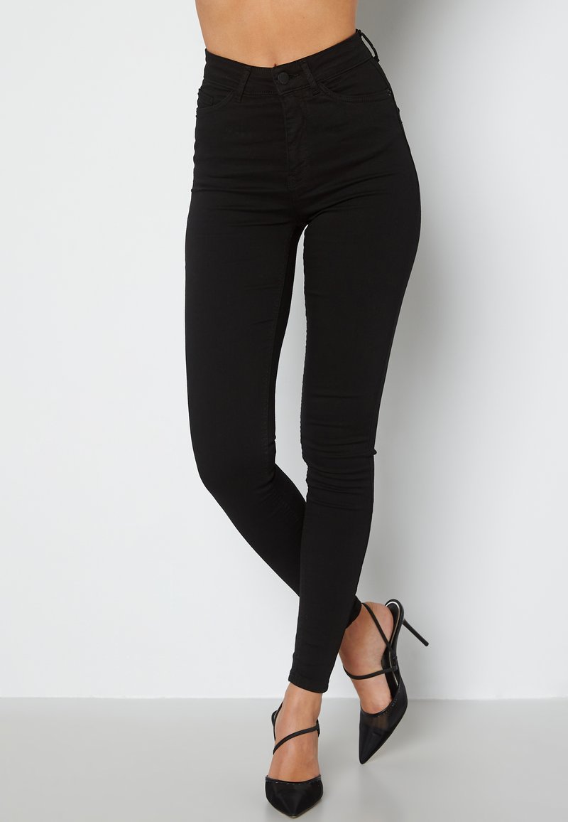 Černé džínové kalhoty s vysokým pasem, úzkého střihu, s hladkým povrchem, zapínáním na zip a pětiprvkovým designem kapes, doplněné o černé špičaté vysoké podpatky.