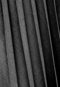 Tissu noir avec des plis verticaux, mettant en valeur une apparence texturée. Le matériau semble doux et a une finition lisse avec des plis réguliers.