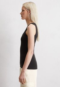 Schwarzes, geripptes Tanktop mit rundem Halsausschnitt und ärmellosem Design, kombiniert mit hellbeigen Hosen, seitlich dargestellt.