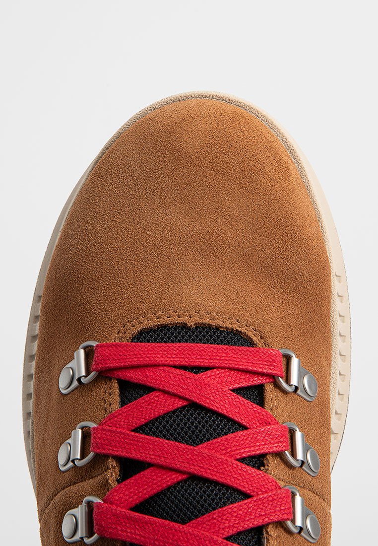 Bruna mockasiner i mocka med röda snören, svart mesh-tunga och silverdetaljer. Rund tå och texturerad sula.