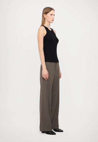Top nero senza maniche abbinato a pantaloni ampi color taupe, caratterizzati da una texture liscia e un design minimalista, completato da scarpe nere a punta.