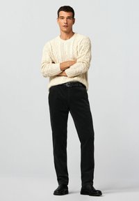 Beiger Strickpullover mit Zopfmuster, kombiniert mit schwarzen Cordhosen. Schwarzer Gürtel und Schuhe vervollständigen das Outfit.