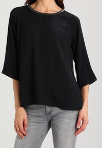 Schwarzes, locker sitzendes Oberteil mit rundem Ausschnitt, Dreiviertelärmeln und akzentuiertem, strukturiertem Ausschnitt. Glattes Material mit leichtem Glanz.
