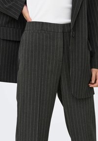 Pantaloni grigi scuri a righe sottili realizzati in un tessuto testurizzato. Presentano un taglio dritto, tasche frontali e una vestibilità su misura.