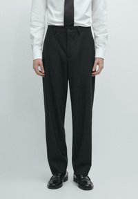 Schwarze, maßgeschneiderte Hose mit weitem Schnitt, glatter Textur, zwei Vordertaschen und einer dezenten Bügelfalte an den Vorderseiten der Beine.