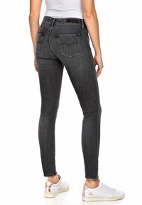 Vaqueros de denim negro ajustados con una cintura de altura media, que cuentan con bolsillos traseros y un ligero aspecto desgastado. Combinados con zapatillas blancas.