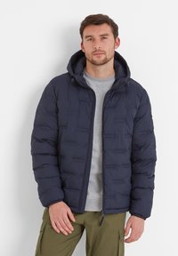 Navy padded jacket with a hood, featuring a zip front and elastic cuffs. Worn over a gray sweater and paired with olive green pants.