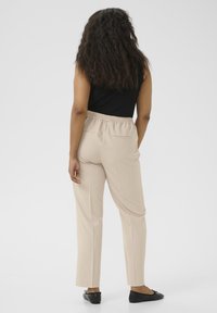 Beige slim-fit pants with elastic waistband, featuring back pockets and a smooth texture, paired with black flat shoes.