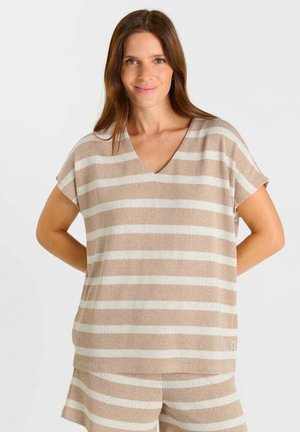 Vrouw met bruin haar draagt een beige-wit horizontaal gestreept topje met korte mouwen en bijpassende korte broek, glimlachend met haar handen achter haar rug.