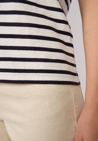 T-shirt rayé en coton blanc et bleu marine. Présente une légère courbure à l'ourlet avec un subtil détail de marque brodé en bas.