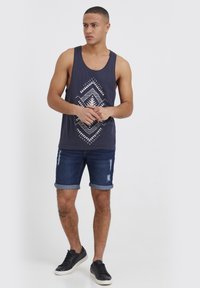 Námornícke tielko s bielym geometrickým vzorom, v kombinácii s potrhanými džínsovými šortkami a čiernymi teniskami, s vyhrnutými manžetami.