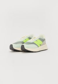 Light green sneakers made of mesh and suede with a bold lime green logo, cream laces, and black rubber soles, featuring a low-profile design.