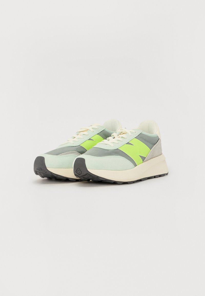 Baskets vert clair en mesh et en suède avec un logo vert lime audacieux, des lacets crème et des semelles en caoutchouc noir, présentant un design bas.