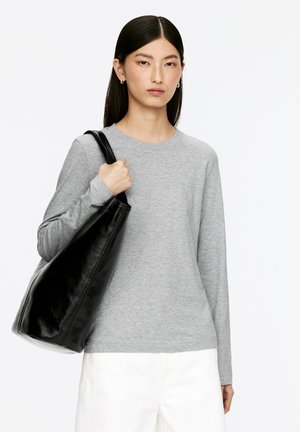 Graues Langarmshirt mit Rundhalsausschnitt, kombiniert mit einer schwarzen Ledertasche. Die Tasche hat eine glatte Textur und eine geschwungene Form.