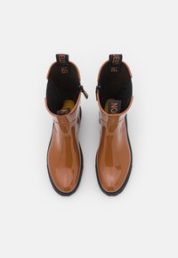 Bottines brillantes marron avec un intérieur noir, des zippers latéraux et des languettes proéminentes marquées "Jelly" et "No". Semelles en caoutchouc texturé.