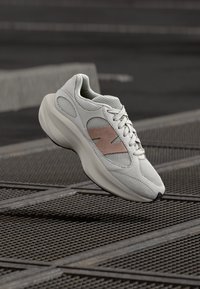 Világosszürke tornacipő hálós és szarvasbőr anyagból, sima, ívelt sziluettel, rózsaszín részletekkel és texturált talppal.