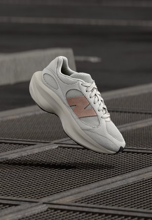 Jasnoszary sneaker wykonany z siateczki i zamszu, o gładkiej, krzywoliniowej sylwetce, różowych akcentach i teksturowanej podeszwie.