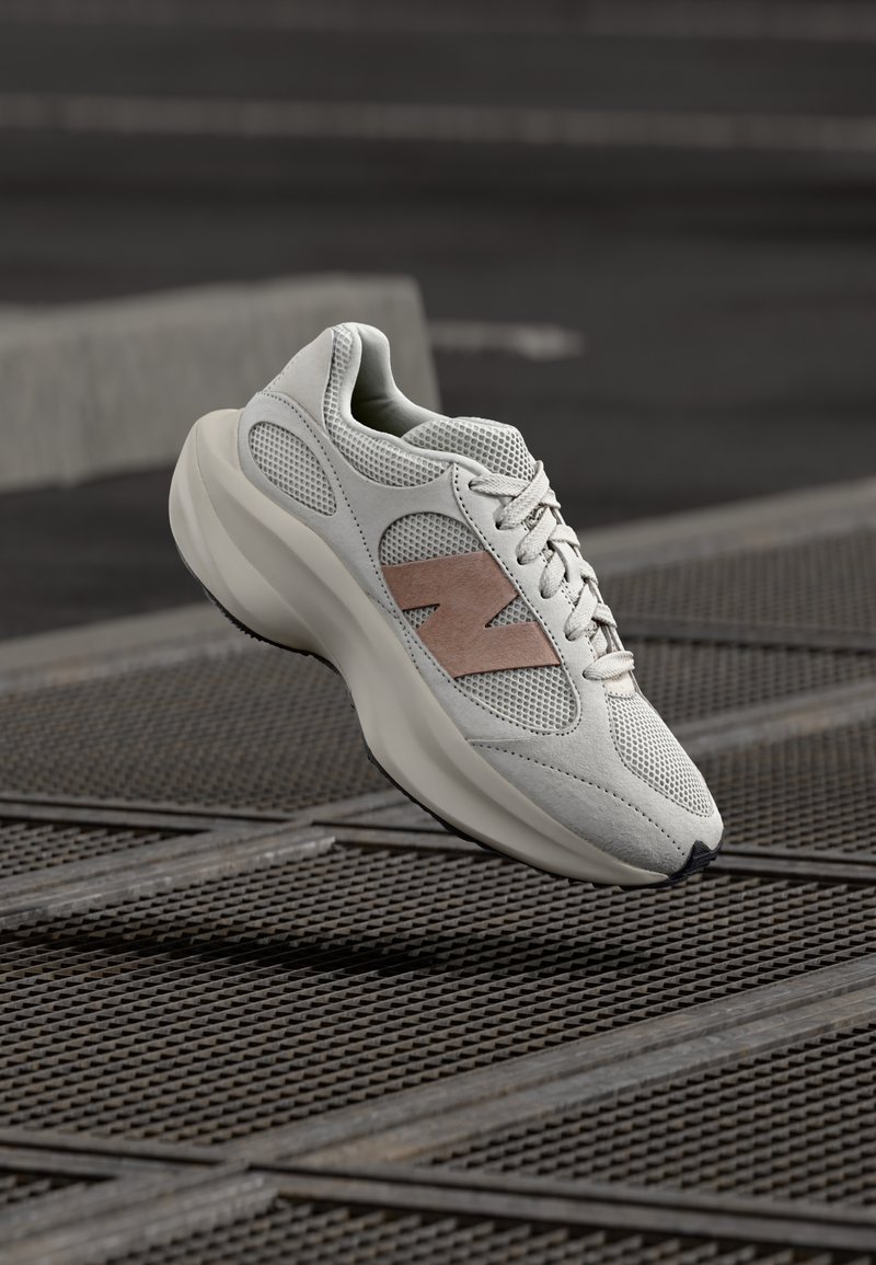 Világosszürke tornacipő hálós és szarvasbőr anyagból, sima, ívelt sziluettel, rózsaszín részletekkel és texturált talppal.