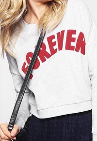 Sudadera gris con la palabra "FOREVER" en letras rojas en negrita, con un diseño corto y una textura suave, combinada con un bolso negro de bandolera.