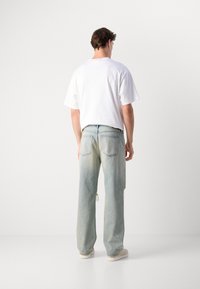 Camiseta de algodón blanca de manga corta, combinada con jeans de denim azul claro desgastados que tienen un aspecto desvanecido y un corte holgado.