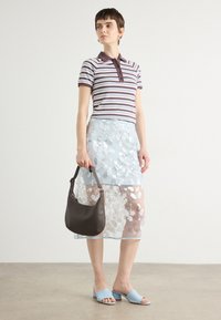 Polo rayé dans des tons frais, jupe légère bleu clair semi-transparente avec des appliqués floraux, sac à main marron, et mules à talons bleues.