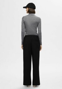 Langermet grå topp med høy krage, parret med svarte vidde bukser og en svart baseballcap. Myk tekstur og avslappet passform.