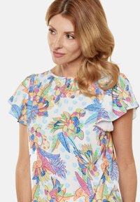 Top floreale a maniche corte con base bianca e vivaci pattern multicolore di foglie e fiori, con scollatura arricciata.