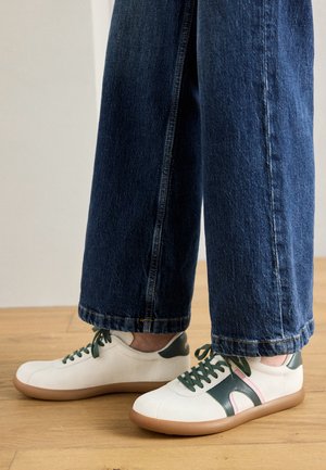 Hvite skinnsneakers med grønne og rosa accenter, teksturert såle og grønne lisser, sammen med mørk denim vide bukser.