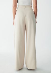 Beige wide-leg pants with a smooth texture, high waist, and tailored design. Features subtle stitching details and a clean, modern silhouette.