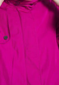 Fuchsia regenjas van glanzende, waterafstotende stof met drukknoopsluiting en opstaande kraag. Heeft verticale naden en een zijzak.