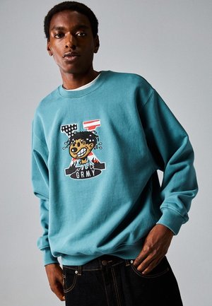 Sudadera turquesa con puños de canalé, que presenta un gráfico de dibujos animados de un personaje sonriente y el texto "GRMY" en negrita negra.