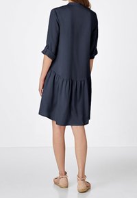 Vestido azul marino oscuro con mangas tres cuartos y dobladillo escalonado, que presenta una textura suave y un sutil detalle en la espalda.