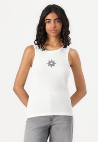 Top de manga curta branco, com decote redondo e um gráfico de sol preto bordado ao centro, combinado com jeans cinza.