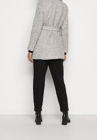 Abrigo texturizado gris con cintura ceñida, con mangas largas y un corte holgado, combinado con pantalones negros y botas de tacón cuadrado.