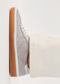 Lysegrå semsket sneakers med hvite aksenter, en teksturert overdel og såle i gommegummi. Lissene er hvite, og skoene er plassert mot en nøytral bakgrunn.