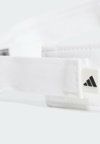 Cinta para la cabeza deportiva de tela blanca con textura suave, que presenta un logo negro de Adidas en una etiqueta blanca. Correa ajustable para un mejor ajuste.